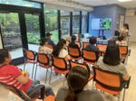 A group of people watching a presentation. A plant is displayed by a projector.