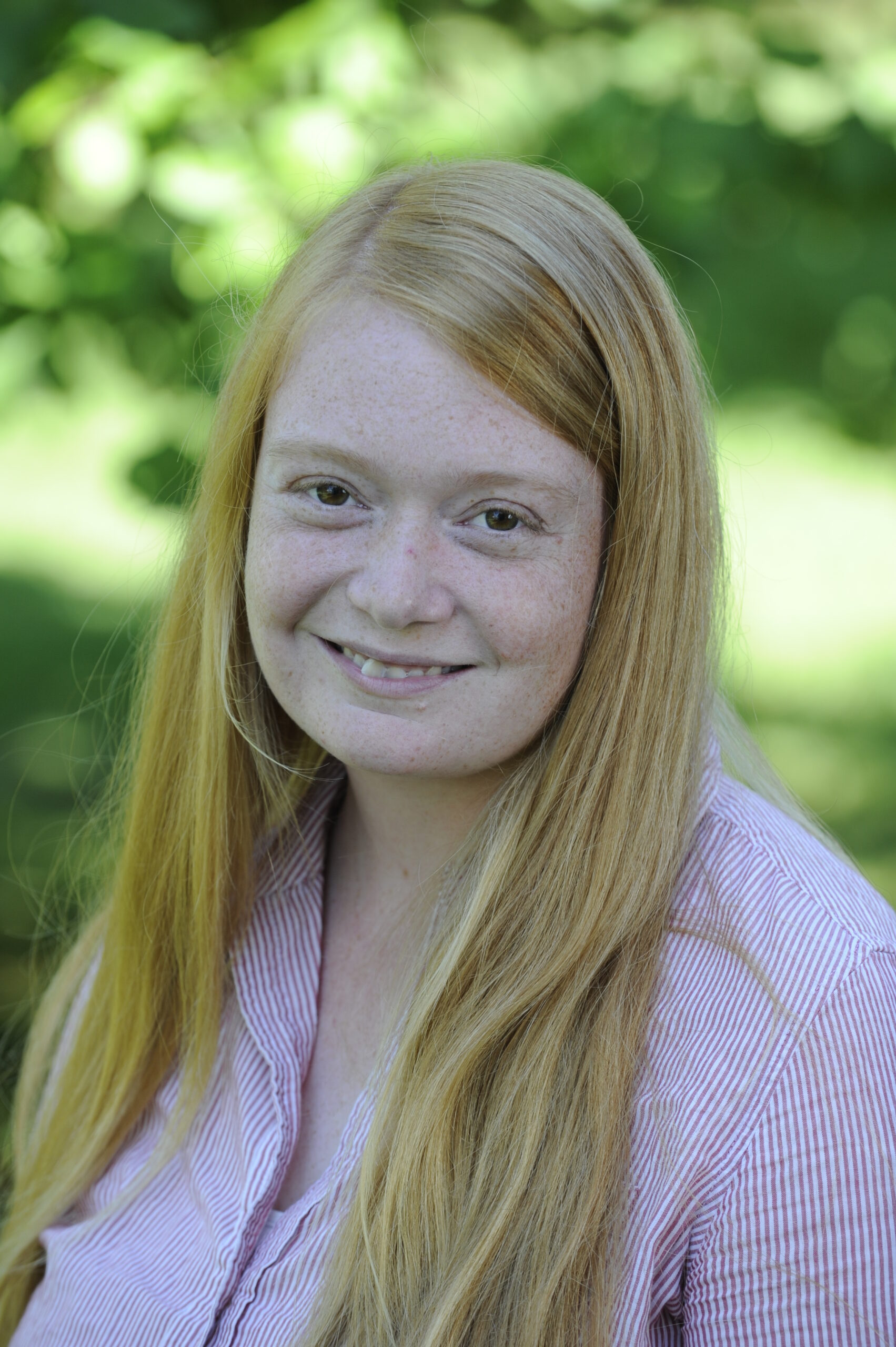 A smiling person outdoors with long hair