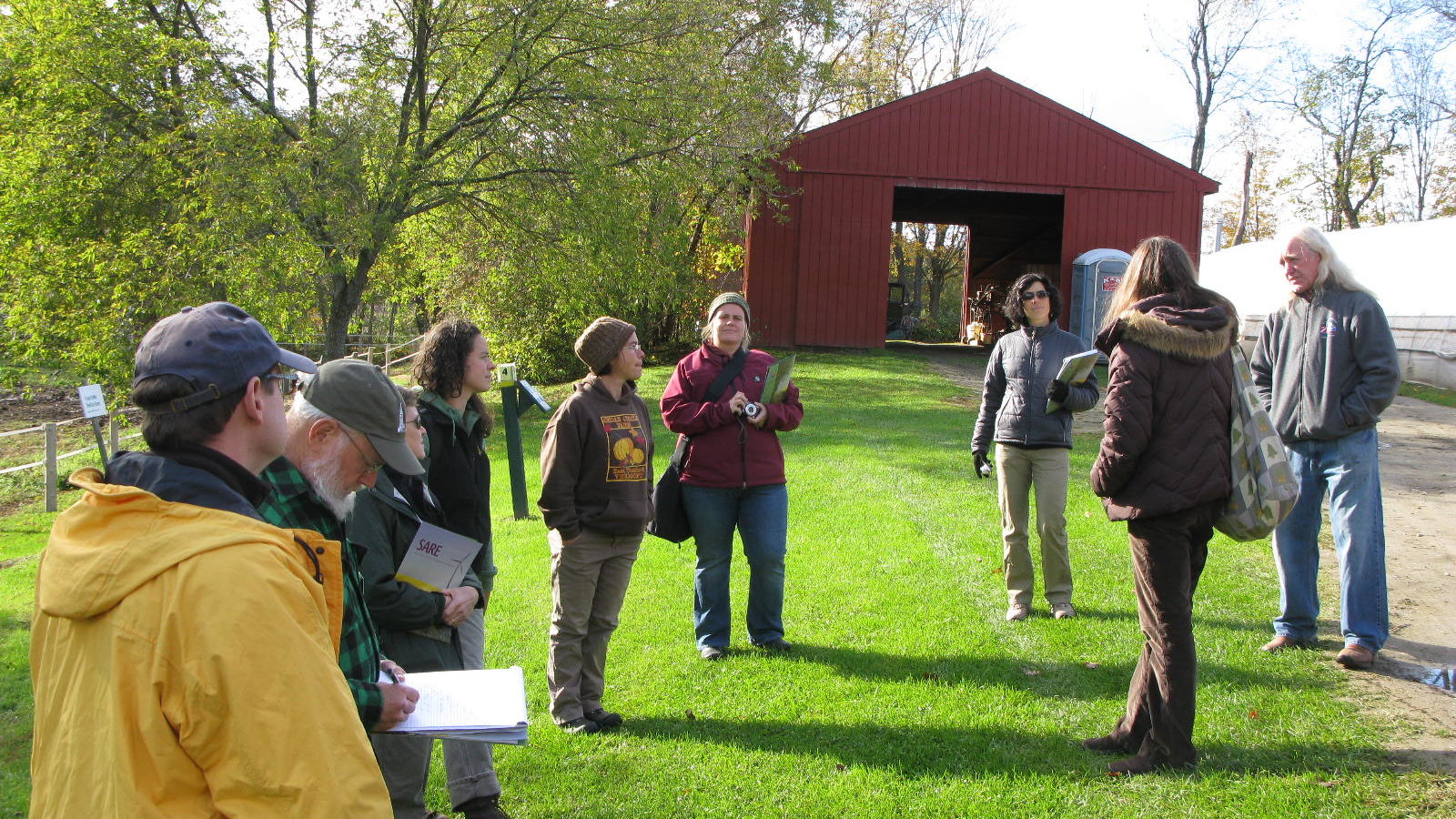 People gathered around outside in winter clothes with a red barn in the background