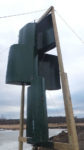 A wind rotor contraption near a pond, with big black metal sheets within a wood frame